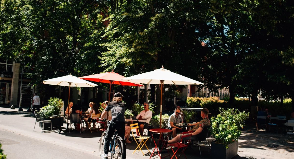 People enjoying a sunny day at a café in Épernay, France, with vibrant umbrellas and greenery.
