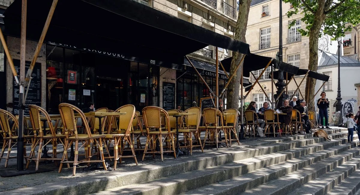 Outdoor Paris café with wicker chairs and people enjoying a sunny day on stone steps.