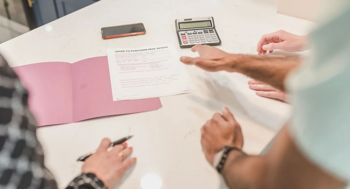 Hands gesturing during a real estate document review on a modern office desk with a calculator.