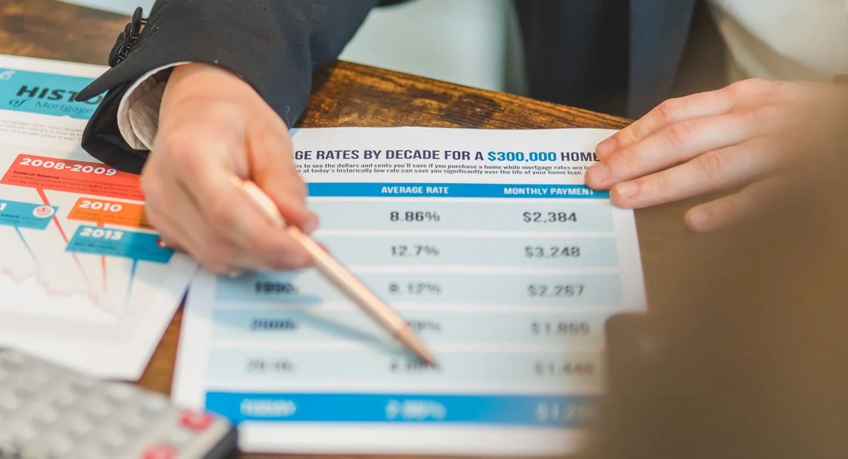 A close-up of hands analyzing mortgage rate documents with a pen and calculator in a business setting.