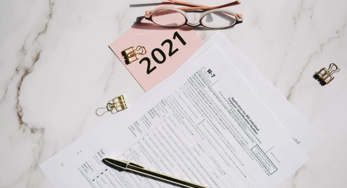 Close-up of W-7 tax forms with glasses and pen on a marble desk, ideal for finance concepts.