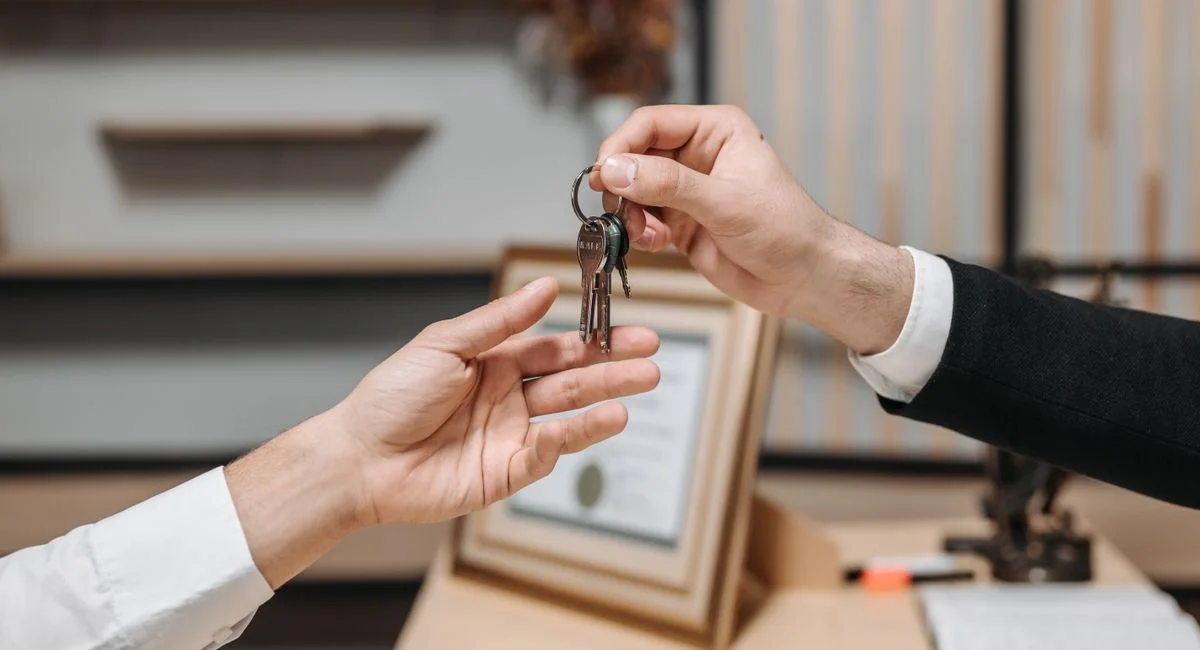 Detailed view of hands exchanging keys in a professional office environment, symbolizing real estate or business transactions