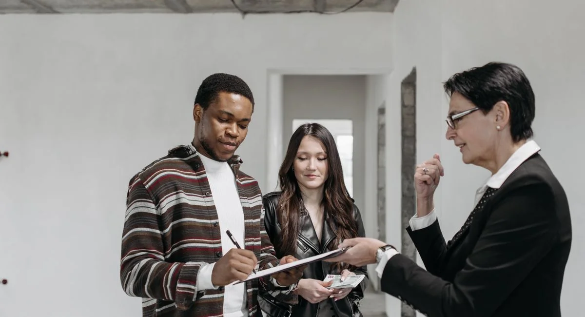 A diverse couple signing documents with a realtor in a new home setting.