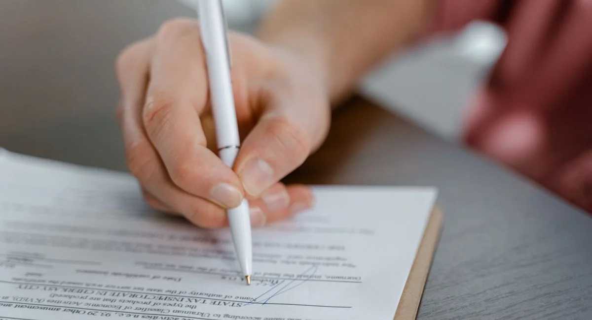 Detailed view of a hand writing a signature on an official document with a ballpoint pen.