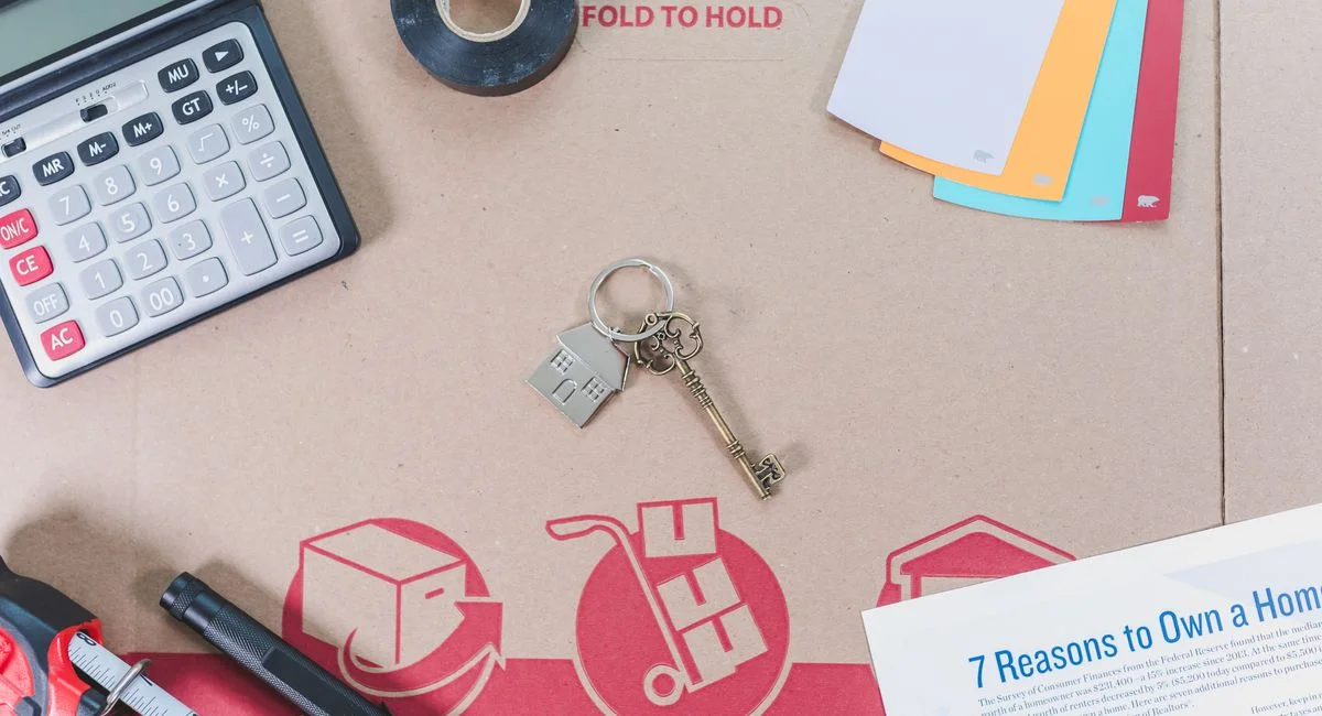 Flat lay of home buying essentials with calculator, keys, tape, and color swatches.