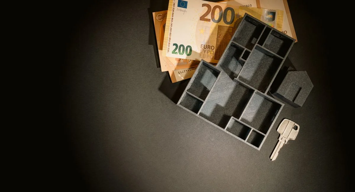 A top view of euro banknotes, a miniature architectural model, and a key symbolizing property investment.