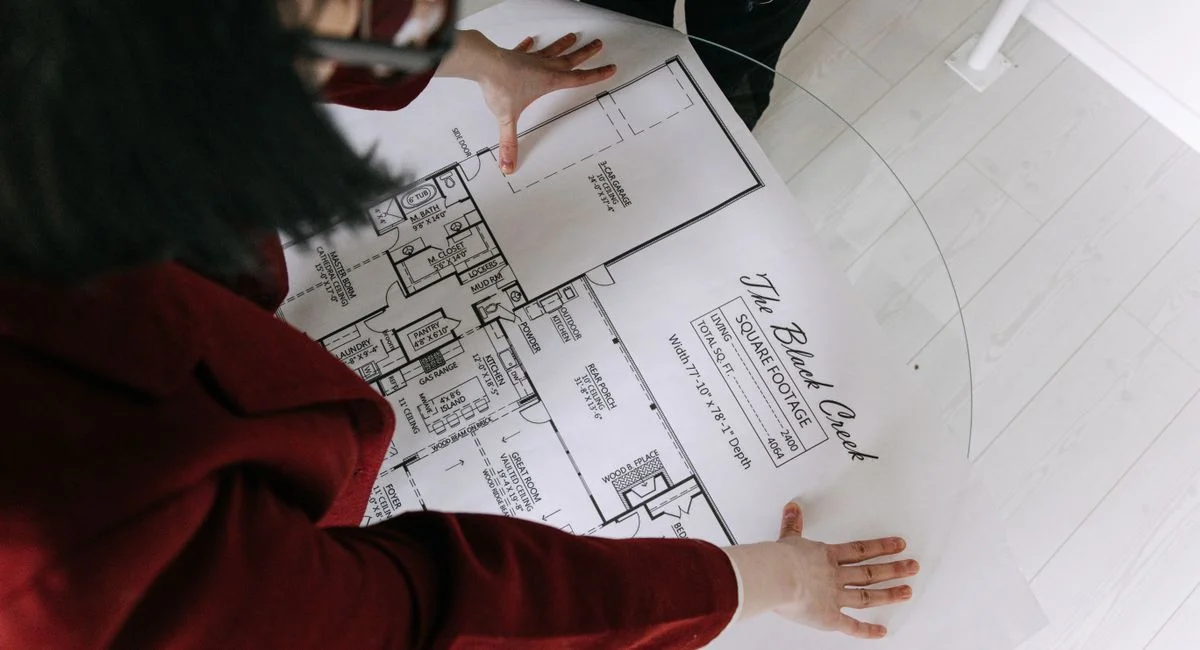 Top view of a woman reviewing detailed architectural blueprints on a glass table, discussing property details.