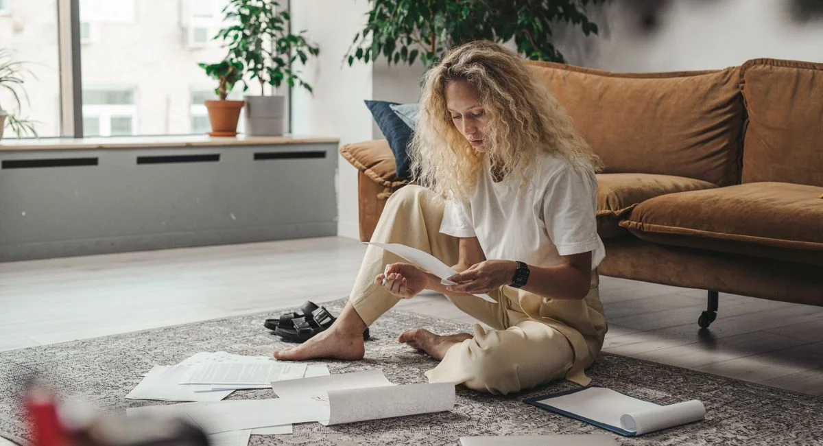 Woman sitting on the floor at home, reviewing paperwork in a relaxed environment.