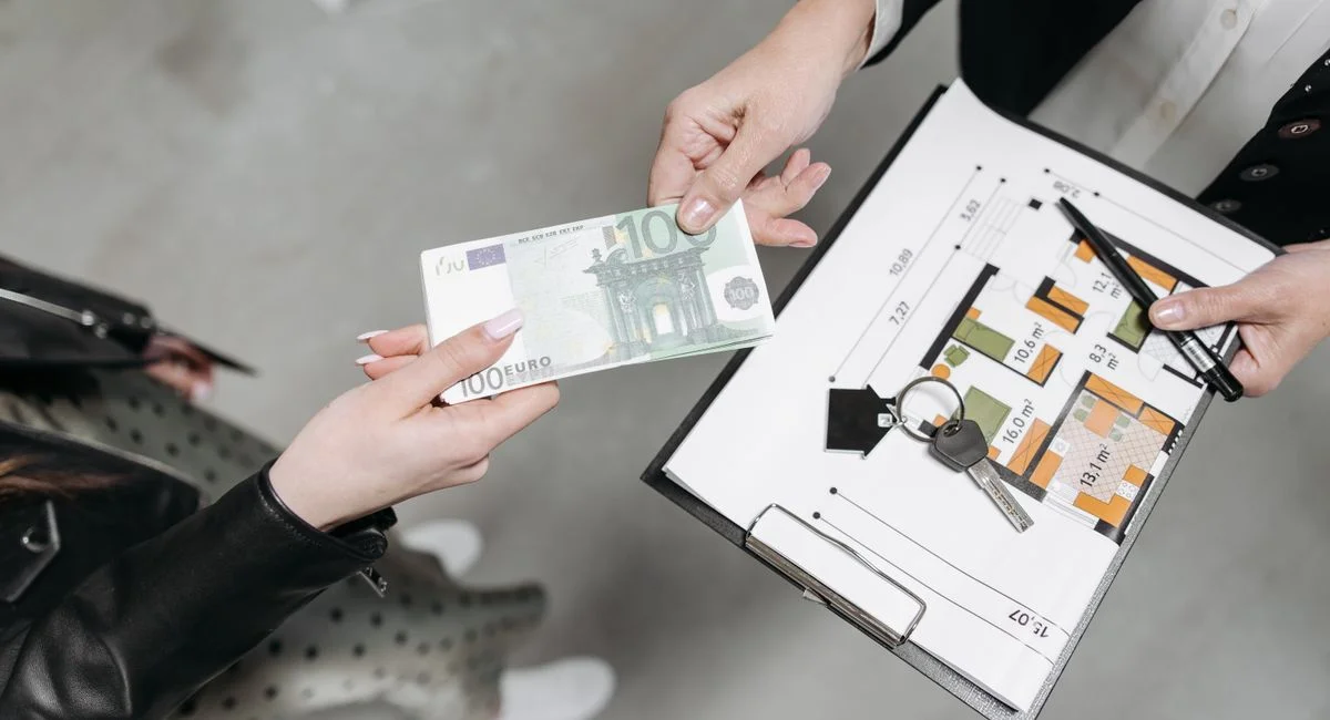 Close-up of a real estate transaction with euro bill, keys, and floor plan.