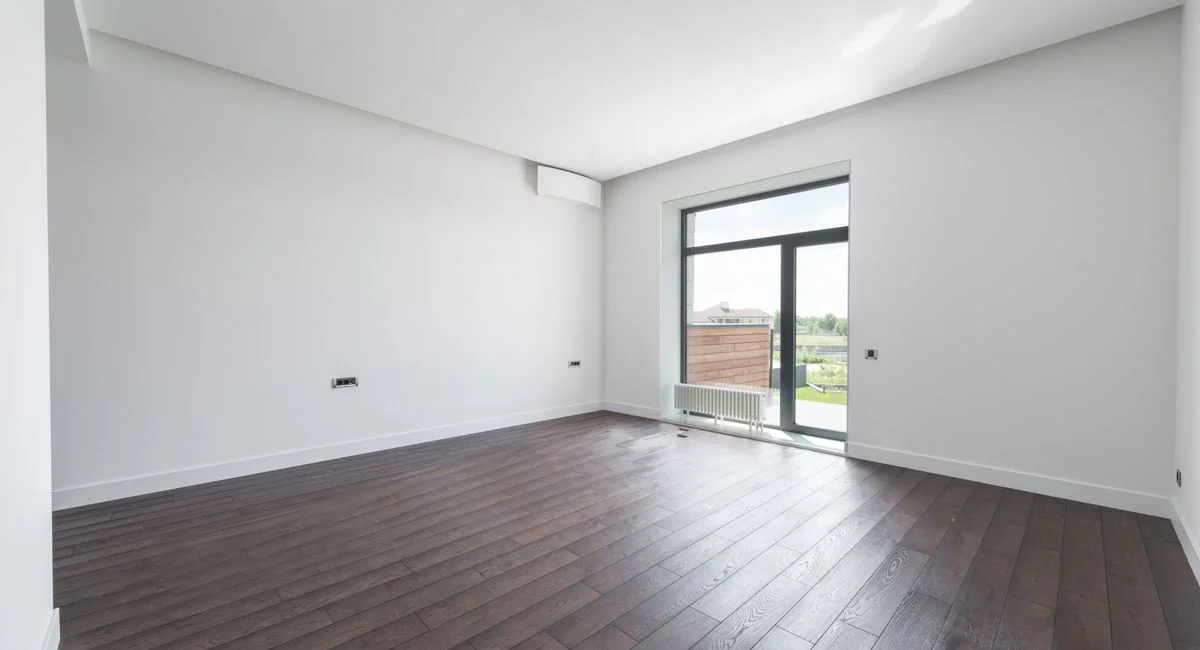Spacious empty room in new apartment with wooden parquet floor and white wall on sunny day
