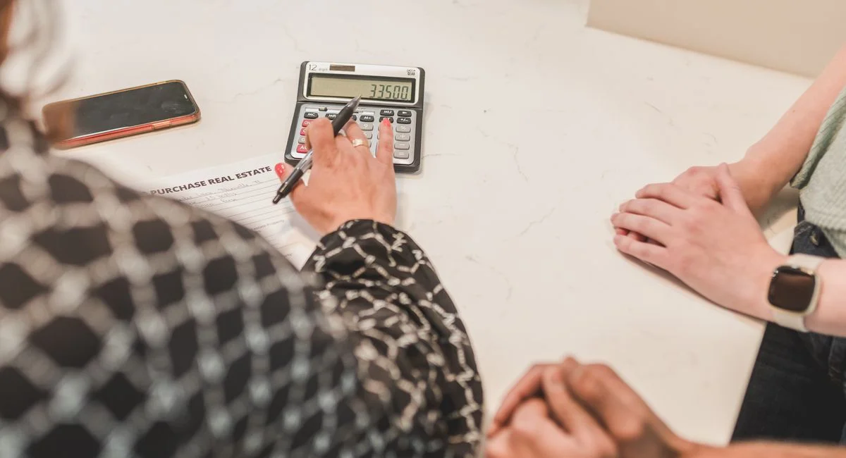 Close-up of hands during a real estate transaction with a calculator and purchase document on the table.