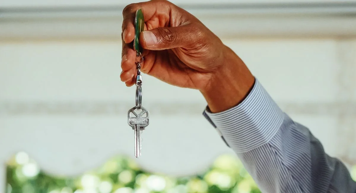 A hand holding a set of house keys, symbolizing buying or renting a new home.