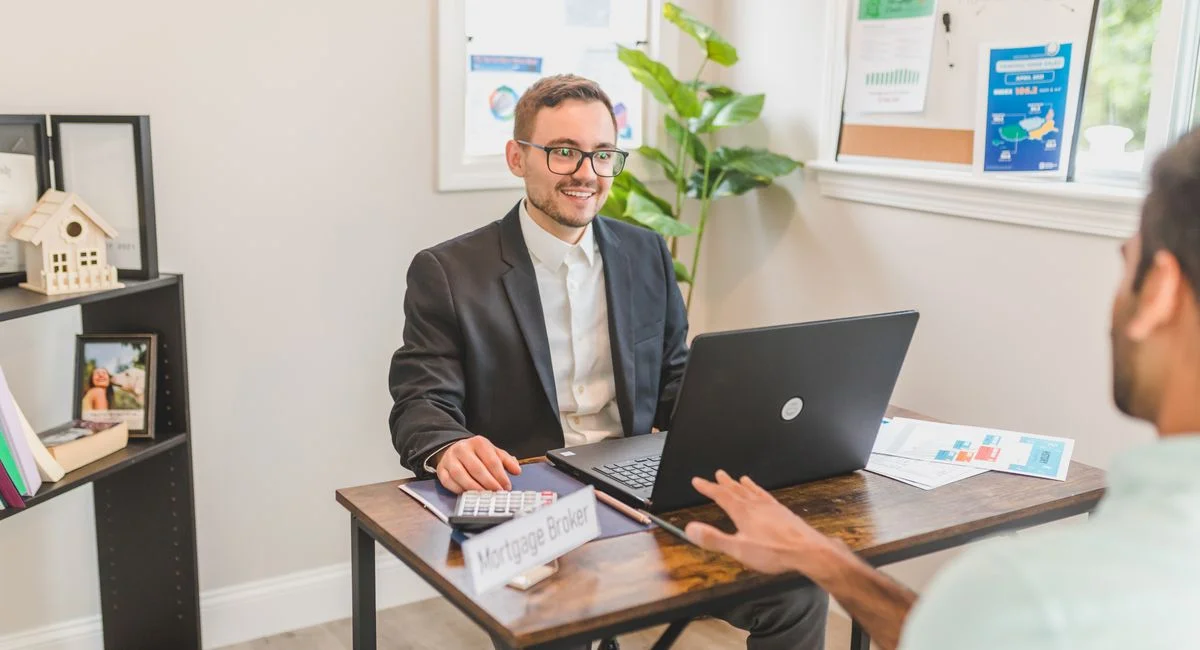 Mortgage broker in an office meeting with a client, utilizing a laptop.