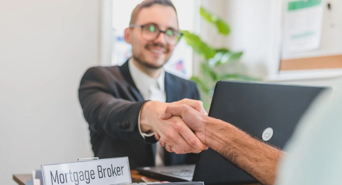Mortgage broker and client sealing a deal with a handshake in a bright, modern office.