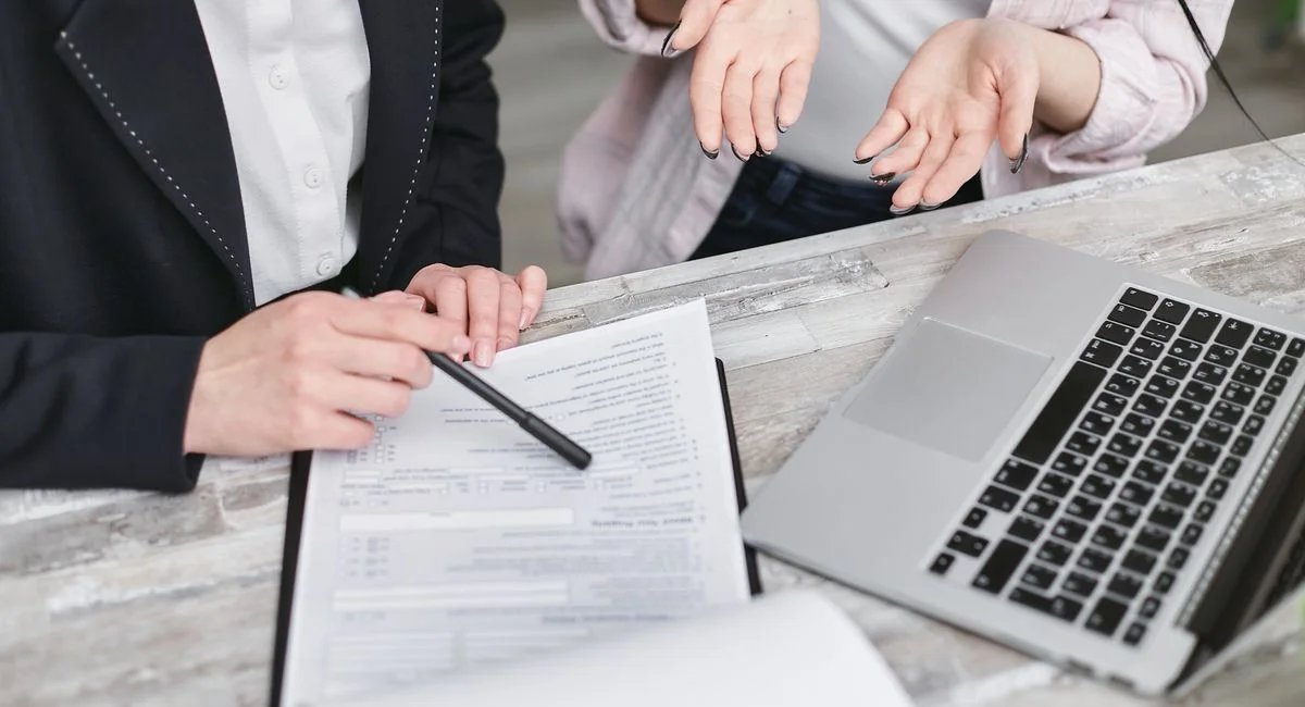 Two professionals discussing a contract at a business meeting with documents and a laptop.