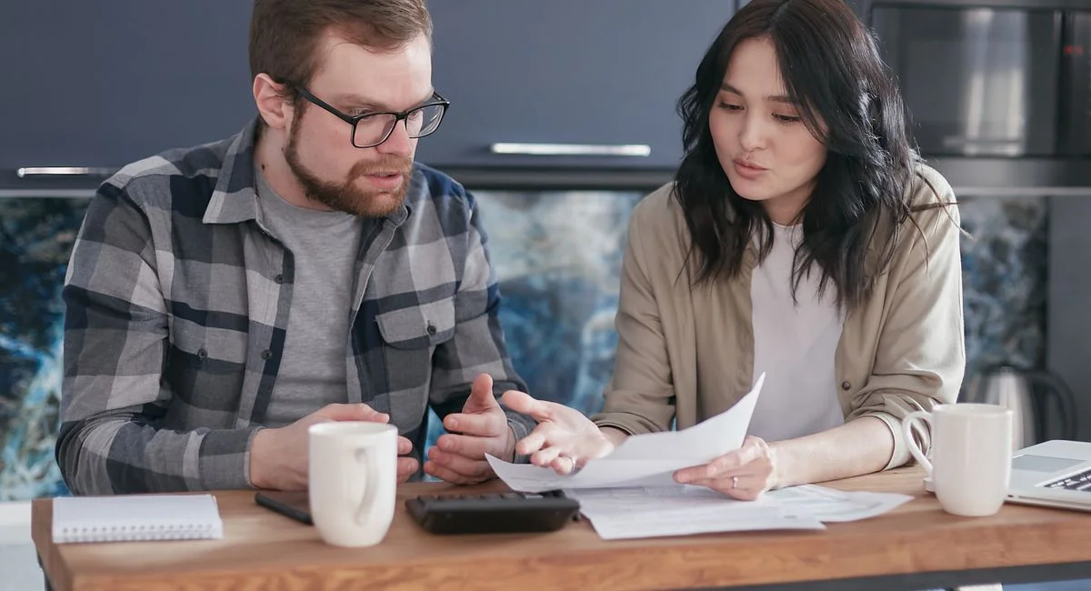 A couple having a serious discussion and reviewing documents at a kitchen table.