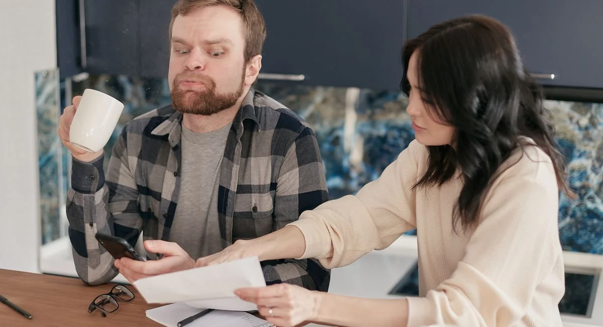 A couple looks worried as they review bills at their kitchen table, reflecting financial concerns.